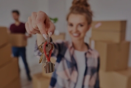 mulher segurando as chaves da sua nova casa com seu companheiro e caixas de mudança ao fundo